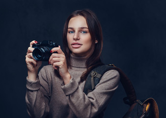 A woman with backpack holds compact photo camera.