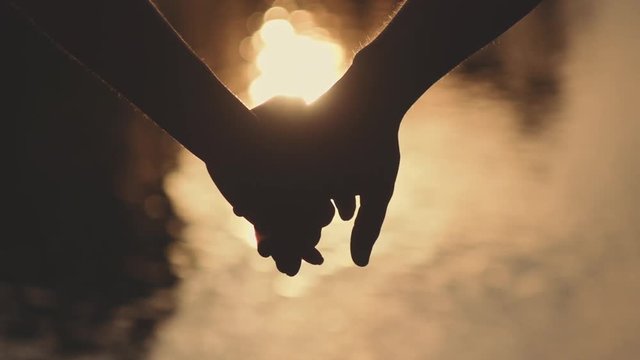 Close up of two Lovers Joining Hands. SLOW MOTION 240 fps. Detail Silhouette of Man and Woman holding hands over the Sunset Lake Background. Couple Trust, Love and Happiness concept. 