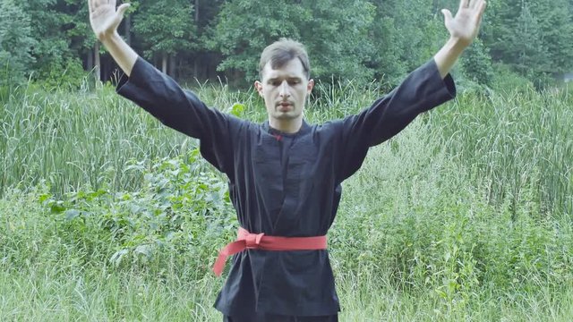 Portrait of a master kung fu in black kimono is relaxing outdoors. Slow motion