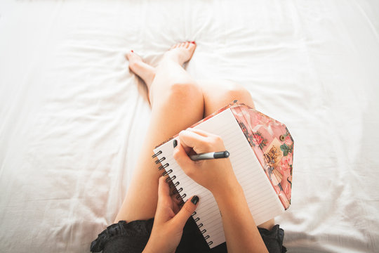 Women sitting in bed with white sheets writing in a notebook.