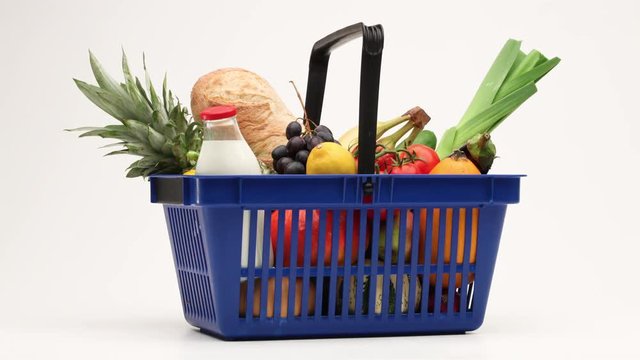 Supermarket shopping basket filled with groceries moving on white background.