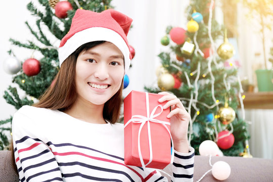 Young cute asian woman wearing santa hat smiling while holding red Christmas gift box, Christmas people celebration concept