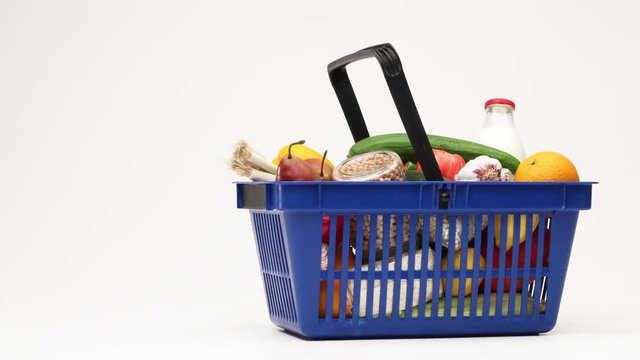 Supermarket shopping basket filled with groceries moving on white background.