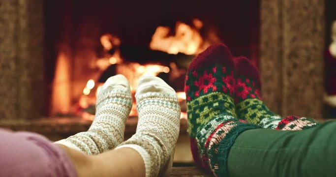 Feet in woolen socks warming by cozy fire in Christmas time in slow motion. Mother and child warming their feet by the fireplace in winter time. Slow motion filmed at 120 fps 4k graded from RAW