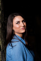 Beautiful smiling young girl leaning against a tree with copy space on black background