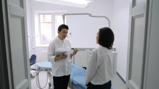 Dentist talking with young female patient in at the dentist clinic.