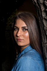 Fototapeta premium Beautiful smiling young girl leaning against a tree with copy space on black background