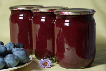 Tkemali Georgian sauce. glass jars with canned sauce. Fresh plums in a plate.