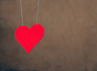 Hung with two chains red metal heart in front of the brown beige wall as a sign for love