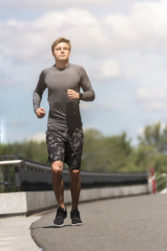 Young jogging man in the city in sportswear in gray color running in urban place, city sunny day.