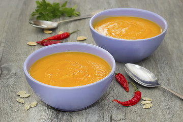 A bright cream soup of pumpkin on a gray wooden table.