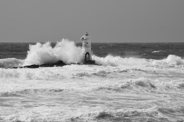 Italy, `Mangiabarche`, Storm. Waves smash against lighthouse or beacon. Black and white