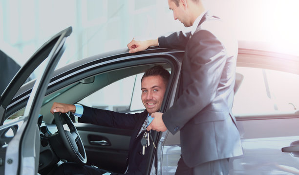 Young man choosing car at salon with help of consultant