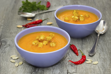 A bright cream soup of pumpkin on a gray wooden table.