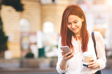 Young woman with coffee to go standing at the street and using mobile phone  