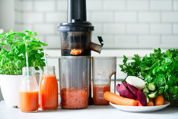 Woman making fresh drink. Juicer and carrot juice. Fruits in background. Clean eating, detox concept