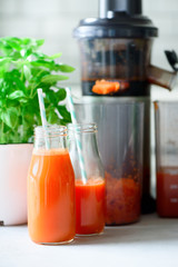 Woman making fresh drink. Juicer and carrot juice. Fruits in background. Clean eating, detox concept