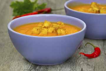 A bright cream soup of pumpkin on a gray wooden table.