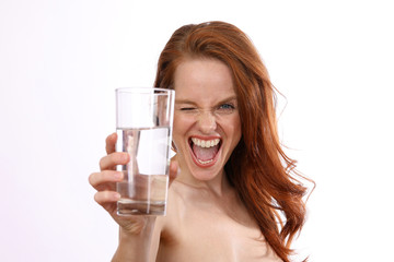 Hübsche rothaarige Frau mit einem Glas Wasser und nackten Schultern lacht