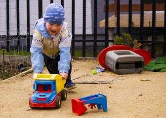 Chłopczyk jeździ zabawkowym autem po placu zabaw przy domu.