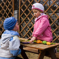 Dziewczynka i chłopiec bawią się piaskiem na ławce w przydomowym placu zabaw.