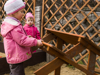 Dziewczynki przewracają ławkę w przydomowym placu zabaw.