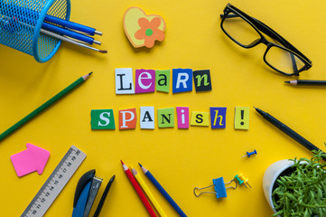 Word LEARN SPANISH made with carved letters on yellow desk with office or school supplies,...