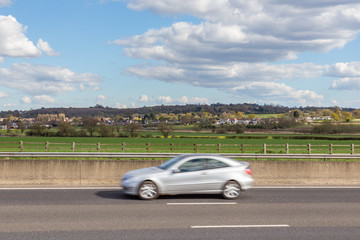 Fototapeta na wymiar Speeding car on the motorway with an Essex village and countryside behind