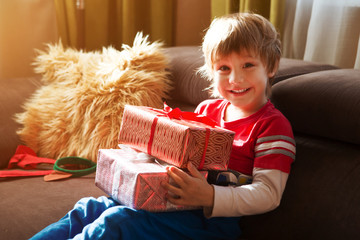 Happy child holding Christmas presents in the morning in the room. Christmas time.  Birthday..