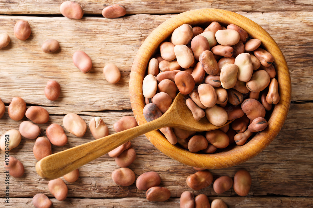 Poster organic broad beans close-up in a wooden bowl on a table. horizontal top view