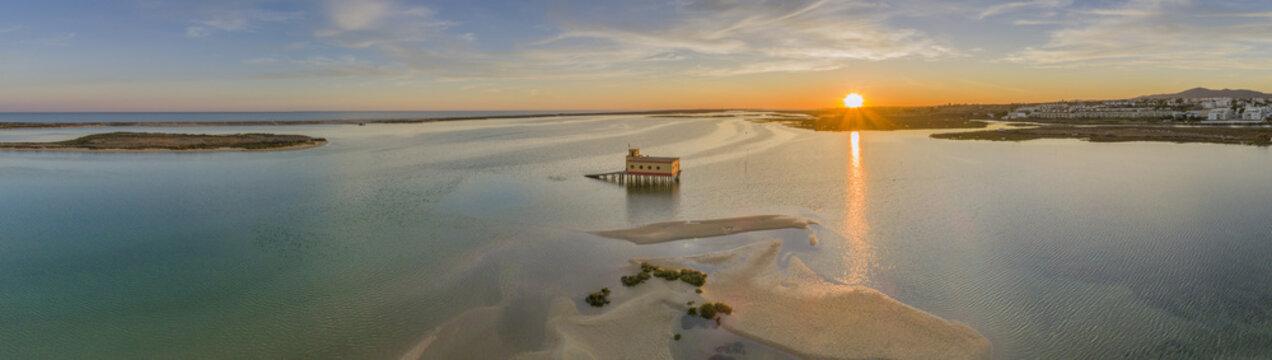 Aerial sunset panoramic and historic life-guard building at Fuseta fishing town, in Ria Formosa wetlands nature conservation park, Algarve. Portugal.