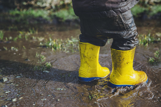 Toddler boy's yellow boots in spring mud puddle - dirty