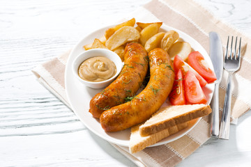 fried pork sausages with potatoes and mustard on white wooden background