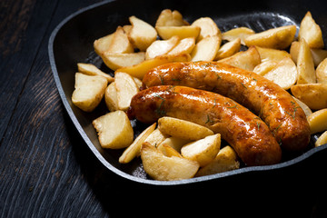 fried pork sausages with potatoes in frying pan