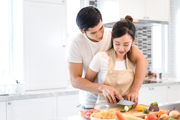 Obraz na płótnie Canvas Couple cooking food in kitchen room, Young Asian man and woman together cutting slice vegetables making each salad for dinner menu with fruits at home romantic indoor sweet lover, copy space the left.