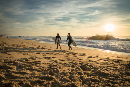enthusiastic surfers going for surf session in scenic beautiful sunset seascape in capbreton, france