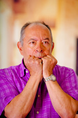 Portrait of a nervous mature man, with both hand in his mouth, wearing a purple square t-shirt in a blurred background