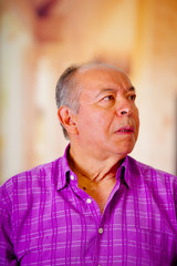 Portrait of a surprissed mature man, with his mouth open and wearing a purple square t-shirt in a blurred background