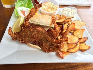 Delicious fried soft shell crab sandwich on sesame seed bun with fresh potato chips, cole slaw, tartar sauce and lemon on a gourmet white plate served at a seaside restaurant