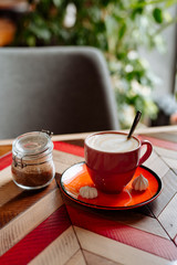 red cup of cappuccino with latte art on old multi-colored rustic table