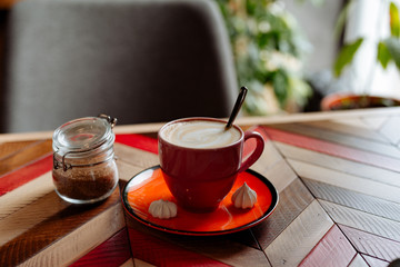 red cup of cappuccino with latte art on old multi-colored rustic table