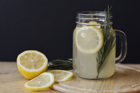 Homemade lemonade with lemon and rosemary leaves in glass jar on wooden table. Healthy drink