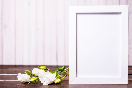 blank photo frame with copyspace and white rose flowers on wooden background. greeting card .