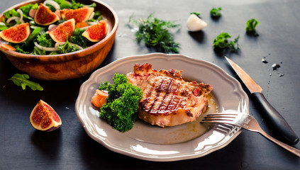 Grilled pork steak and autumn salad with fig on black background.