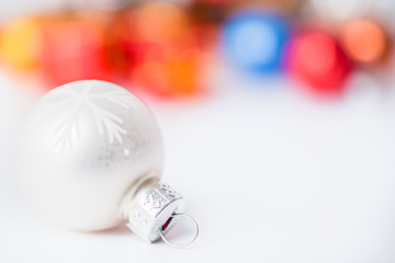 Close-up of white xmas ball with blurred colorful Christmas decor in background. Christmas and New Year concept with copy space. Christmas greeting card.