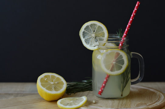Lemonade with rosemary and lemon in glass jar with red straw served on wooden table