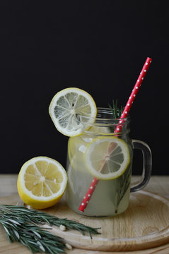 Glass cocktail jar with lemonade with rosemary and lemon slices decorated with red straw and served on wooden table