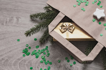 A Christmas shopping bag with a gift in a golden box, a fur-tree branch, a silver star and a green candy.