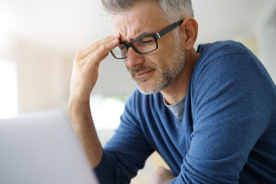 Man at home having a headache in front of laptop