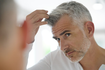 40-year-old man checking hair in front of mirror - obrazy, fototapety, plakaty